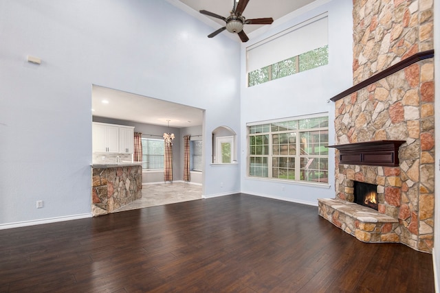 unfurnished living room featuring ceiling fan with notable chandelier, a high ceiling, hardwood / wood-style floors, and a stone fireplace