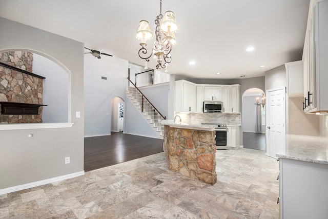 kitchen with pendant lighting, backsplash, white cabinetry, stainless steel appliances, and a fireplace