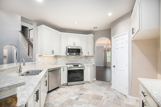 kitchen with stainless steel appliances, white cabinets, light stone counters, and sink