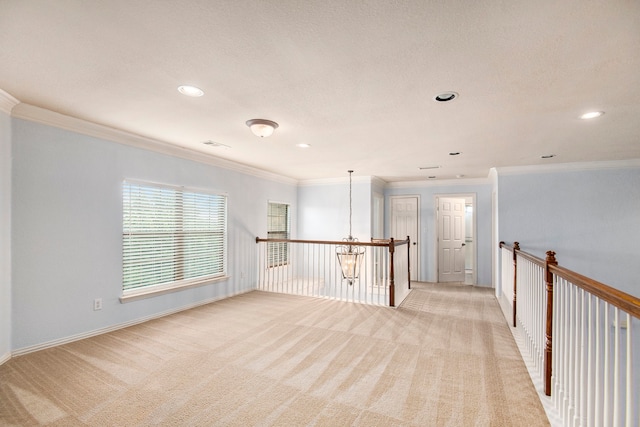 carpeted spare room with an inviting chandelier, a textured ceiling, and ornamental molding