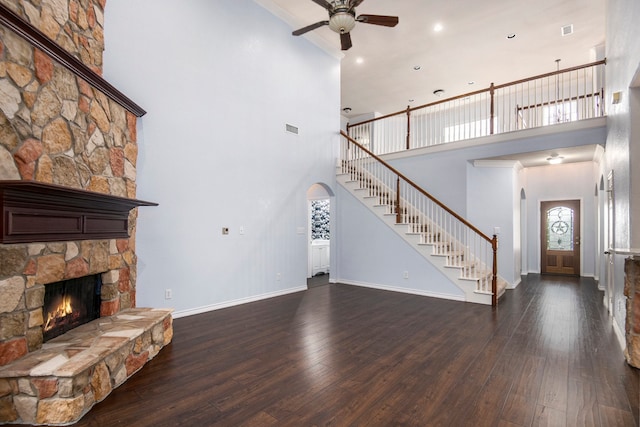 unfurnished living room with a fireplace, a towering ceiling, ceiling fan, and dark wood-type flooring