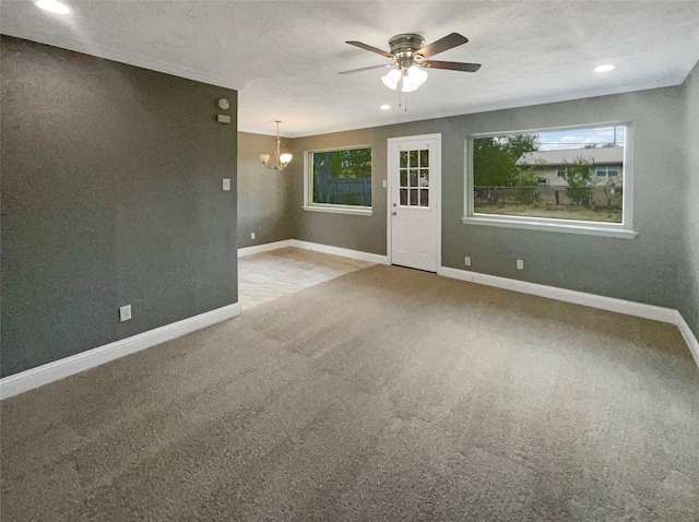 carpeted empty room with ceiling fan with notable chandelier and a textured ceiling