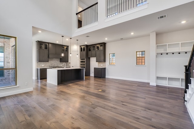 kitchen with a kitchen island with sink, visible vents, open floor plan, and dark wood-type flooring