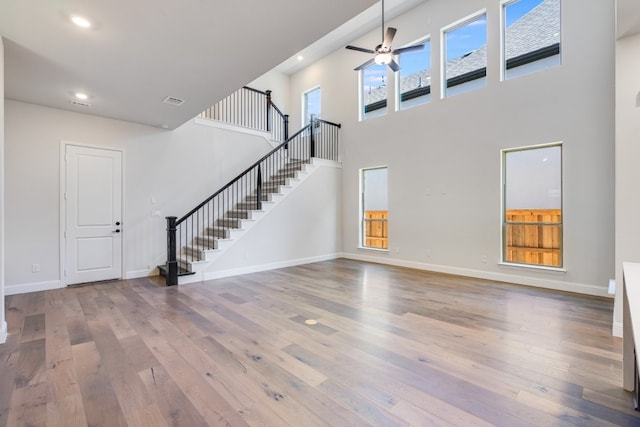 unfurnished living room with baseboards, a towering ceiling, stairway, wood finished floors, and recessed lighting