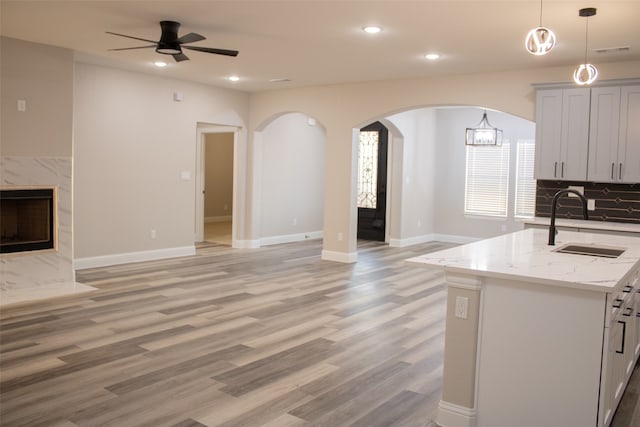 kitchen featuring light stone countertops, an island with sink, light wood-type flooring, white cabinetry, and ceiling fan with notable chandelier