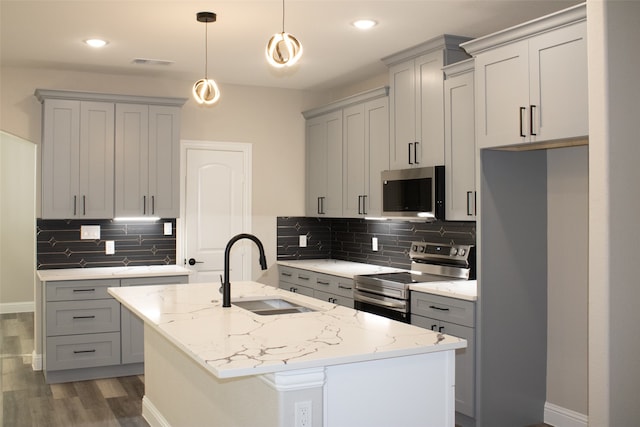 kitchen with appliances with stainless steel finishes, a center island with sink, light stone countertops, and decorative light fixtures