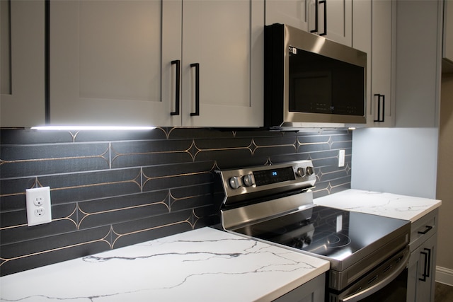 kitchen featuring light stone counters, gray cabinets, stainless steel appliances, and tasteful backsplash