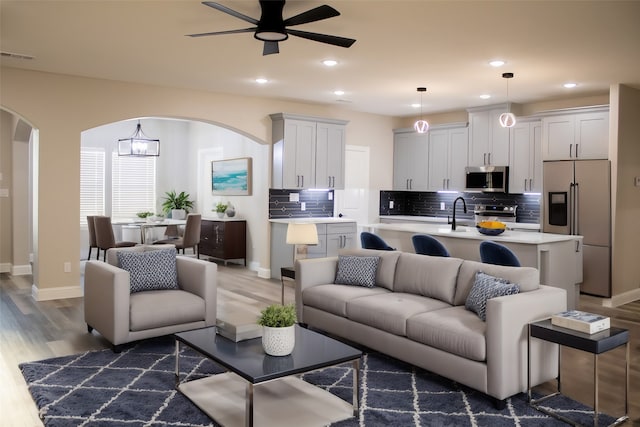 living room featuring sink, ceiling fan with notable chandelier, and dark wood-type flooring