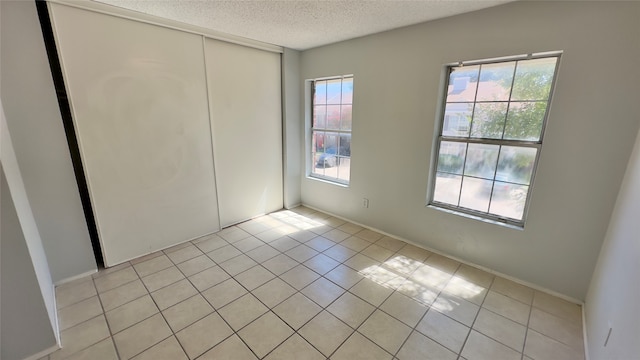 unfurnished bedroom with a textured ceiling, light tile patterned floors, and a closet