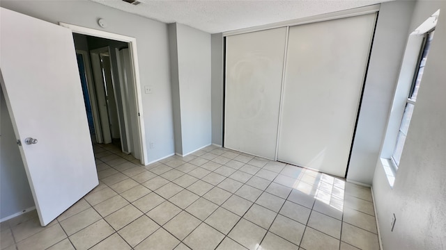 unfurnished bedroom featuring a textured ceiling, light tile patterned floors, and a closet