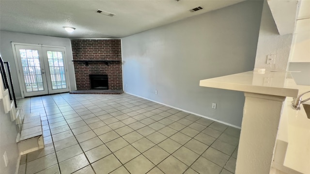 unfurnished living room featuring french doors, light tile patterned flooring, a brick fireplace, and a textured ceiling