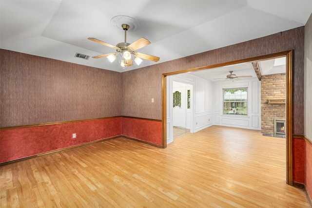 unfurnished room featuring light hardwood / wood-style floors, a fireplace, vaulted ceiling, and ceiling fan