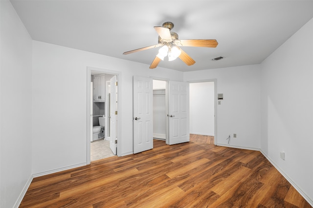 unfurnished bedroom with ceiling fan, a walk in closet, ensuite bathroom, and dark wood-type flooring