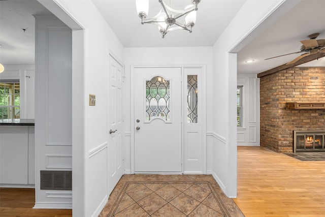 foyer entrance featuring ceiling fan with notable chandelier, a brick fireplace, and hardwood / wood-style floors