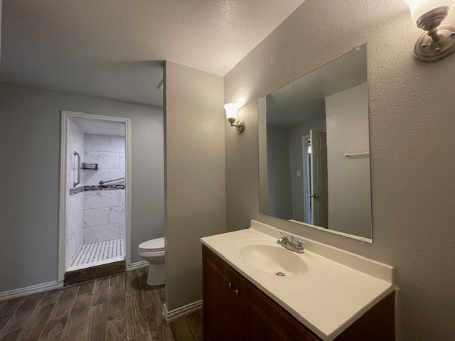 bathroom featuring wood-type flooring, vanity, a tile shower, and toilet