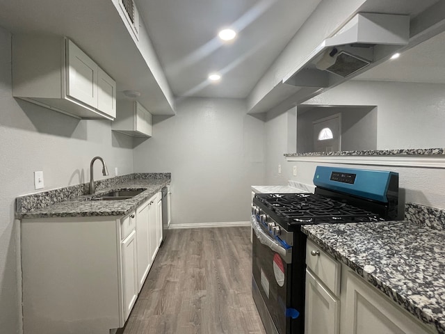 kitchen with white cabinets, sink, wood-type flooring, stainless steel gas range oven, and dark stone countertops