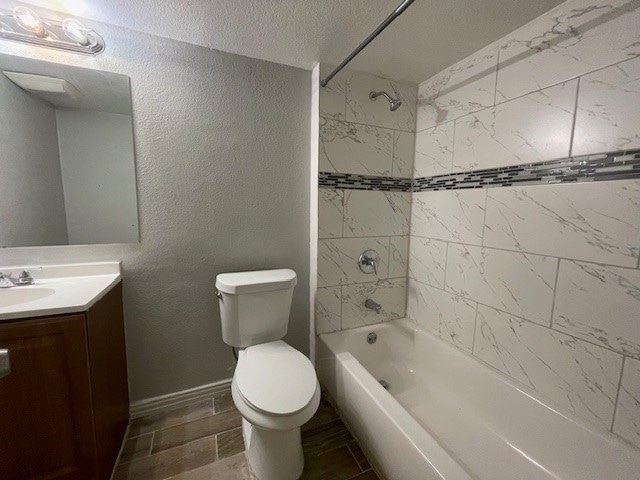 full bathroom with a textured ceiling, tiled shower / bath combo, vanity, and toilet