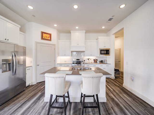 kitchen with a center island with sink, appliances with stainless steel finishes, dark wood-type flooring, and white cabinetry