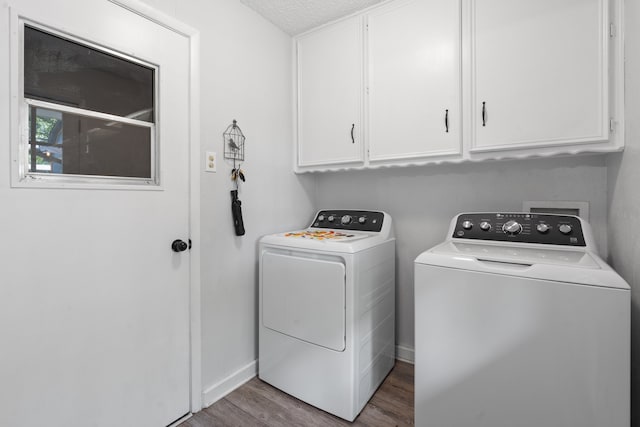 clothes washing area featuring a textured ceiling, wood-type flooring, washing machine and clothes dryer, and cabinets