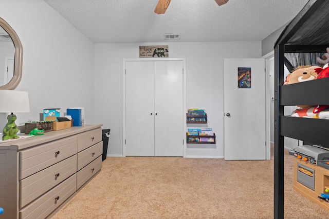 bedroom featuring ceiling fan, light colored carpet, a textured ceiling, and a closet