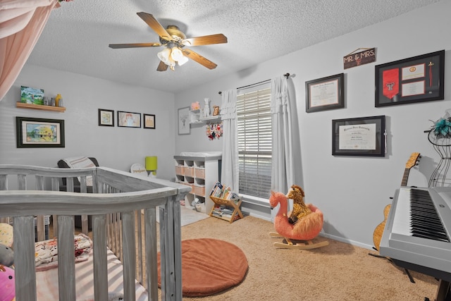 bedroom with ceiling fan, a nursery area, a textured ceiling, and carpet flooring