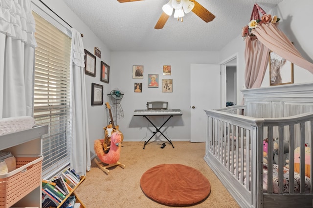 carpeted bedroom with a crib, a textured ceiling, and ceiling fan