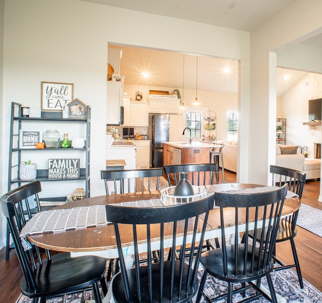 dining area with a stone fireplace, vaulted ceiling, sink, and dark wood-type flooring