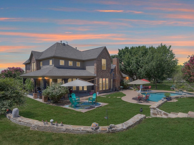 pool at dusk featuring a yard and a patio