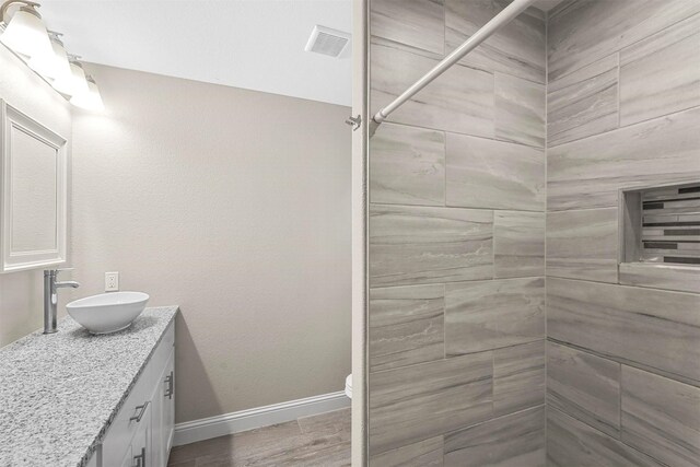 full bath featuring visible vents, baseboards, wood finished floors, tiled shower, and vanity