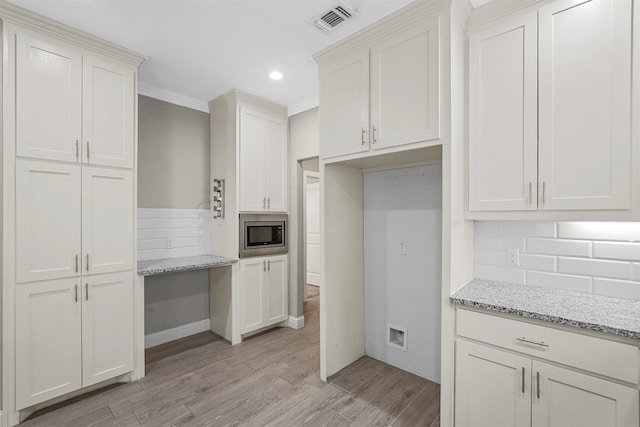 kitchen featuring light hardwood / wood-style floors, white cabinetry, light stone counters, stainless steel microwave, and ornamental molding