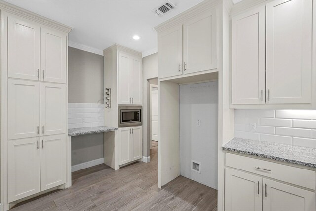 kitchen featuring visible vents, light wood finished floors, stainless steel microwave, tasteful backsplash, and light stone counters