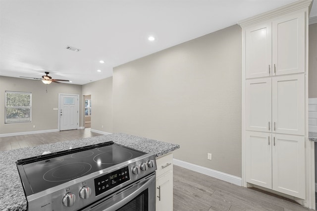 kitchen with white cabinets, light stone countertops, stainless steel range oven, light hardwood / wood-style flooring, and ceiling fan