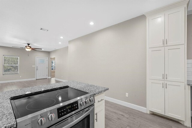 kitchen with light stone counters, light wood-style floors, visible vents, electric range, and ceiling fan