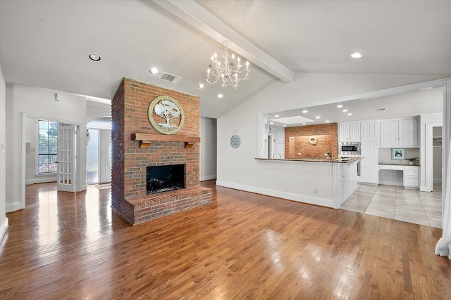 unfurnished living room featuring lofted ceiling with beams, a chandelier, a fireplace, and light hardwood / wood-style floors