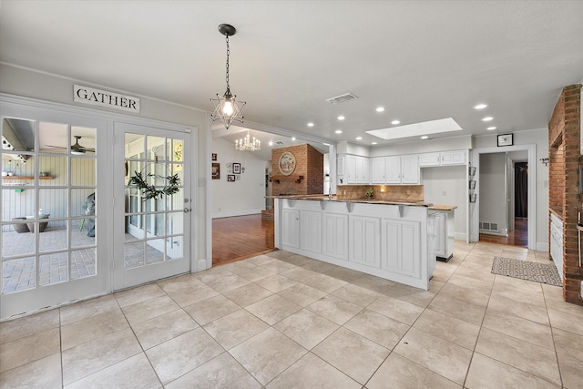 kitchen featuring backsplash, a skylight, pendant lighting, light tile patterned floors, and white cabinets