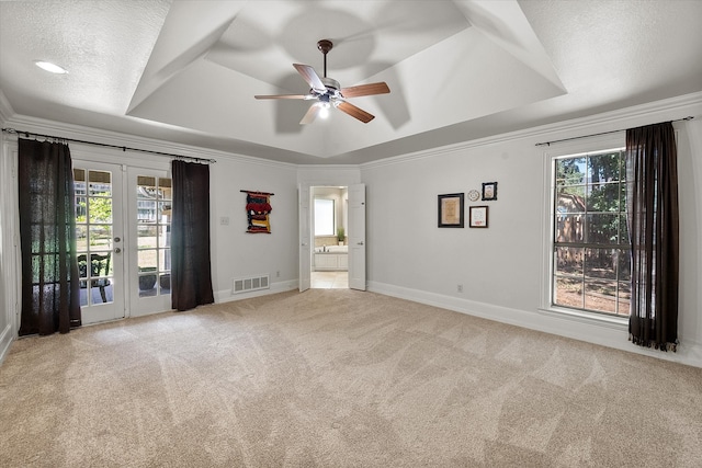 interior space with a raised ceiling, multiple windows, ceiling fan, and french doors