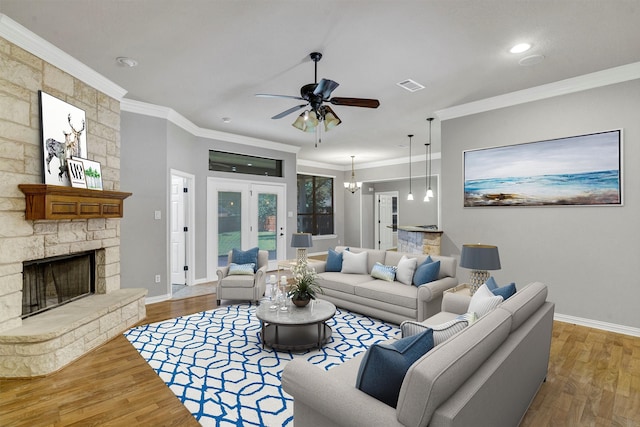 living room featuring hardwood / wood-style flooring, ceiling fan with notable chandelier, crown molding, and a fireplace