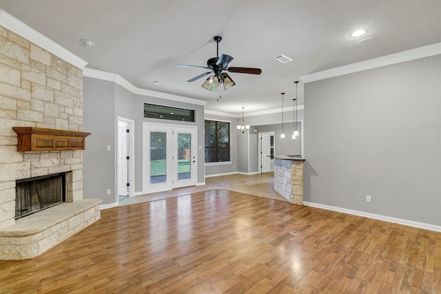 unfurnished living room featuring ornamental molding, light wood-type flooring, ceiling fan with notable chandelier, and a stone fireplace