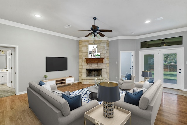 living room featuring light hardwood / wood-style floors, crown molding, ceiling fan, and a stone fireplace