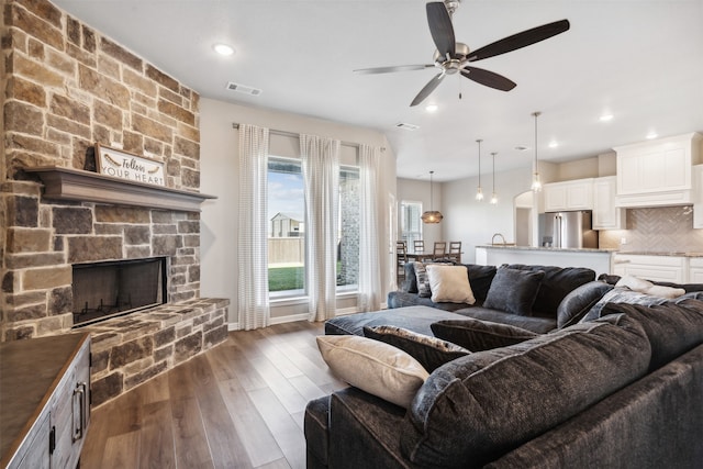 living room with ceiling fan, a stone fireplace, and dark hardwood / wood-style flooring