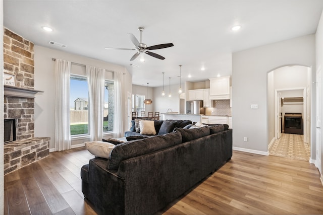 living room with ceiling fan, a stone fireplace, and light hardwood / wood-style flooring