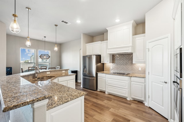 kitchen with light hardwood / wood-style floors, a large island with sink, white cabinetry, stainless steel appliances, and sink