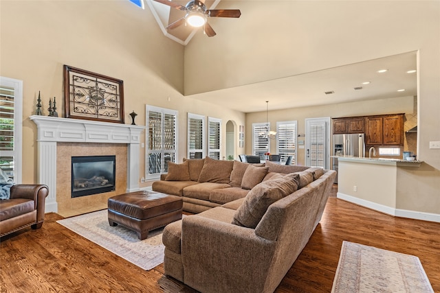 living room with ceiling fan, a fireplace, dark hardwood / wood-style floors, and a towering ceiling