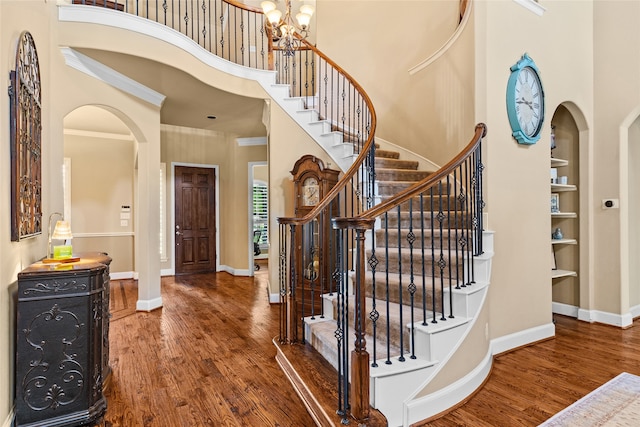 foyer entrance featuring an inviting chandelier, a towering ceiling, hardwood / wood-style flooring, and ornamental molding