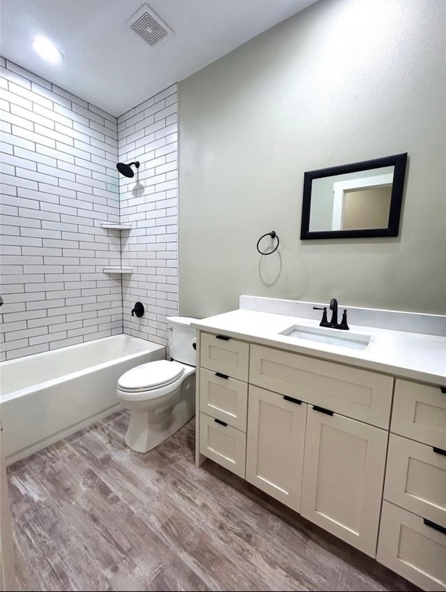 full bathroom with hardwood / wood-style floors, tiled shower / bath, vanity, and toilet