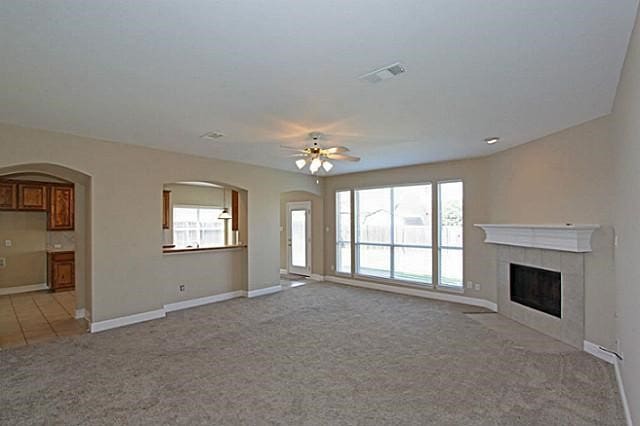 unfurnished living room with ceiling fan, light colored carpet, and a tiled fireplace