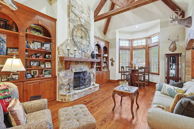 living room featuring high vaulted ceiling, light hardwood / wood-style floors, beamed ceiling, and a fireplace