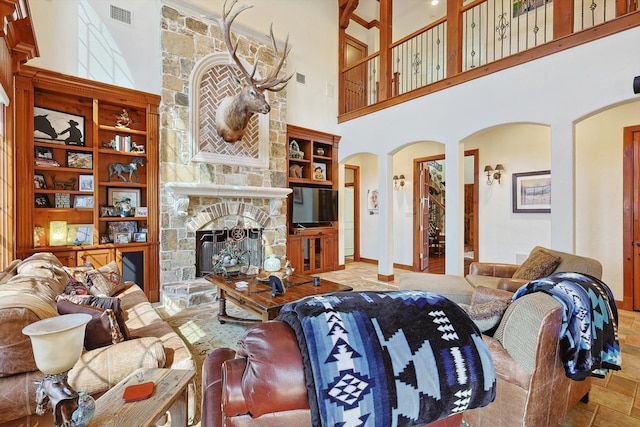 living room with ornate columns, a towering ceiling, and a stone fireplace