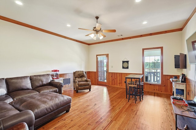 living room with wooden walls, light hardwood / wood-style floors, ceiling fan, and crown molding