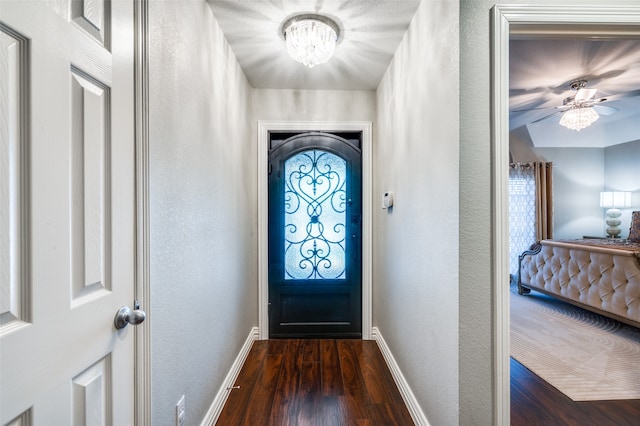 doorway with ceiling fan with notable chandelier and dark wood-type flooring